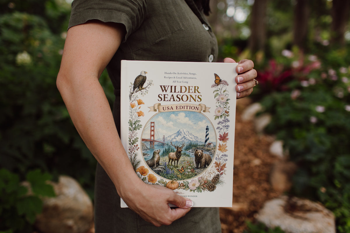 Woman holding the Wilder Seasons USA Family Edition guidebook outdoors
